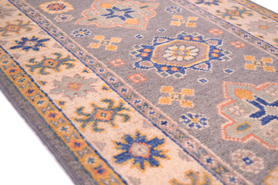 A close-up of a patterned small runner with a grey field, beige border, and blue and orange geometric medallions.