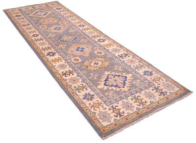 A long rectangular Kazak strip with an intricate traditional pattern in muted blue, beige, orange, and gray tones, shown on a plain white background.
