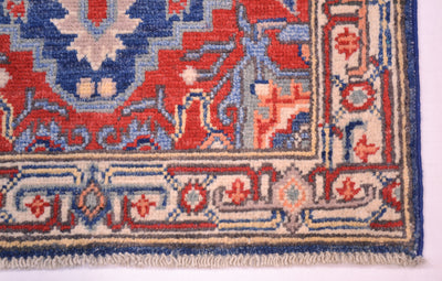 Corner detail of Kazak rug with blue and red motifs and cream border trim.