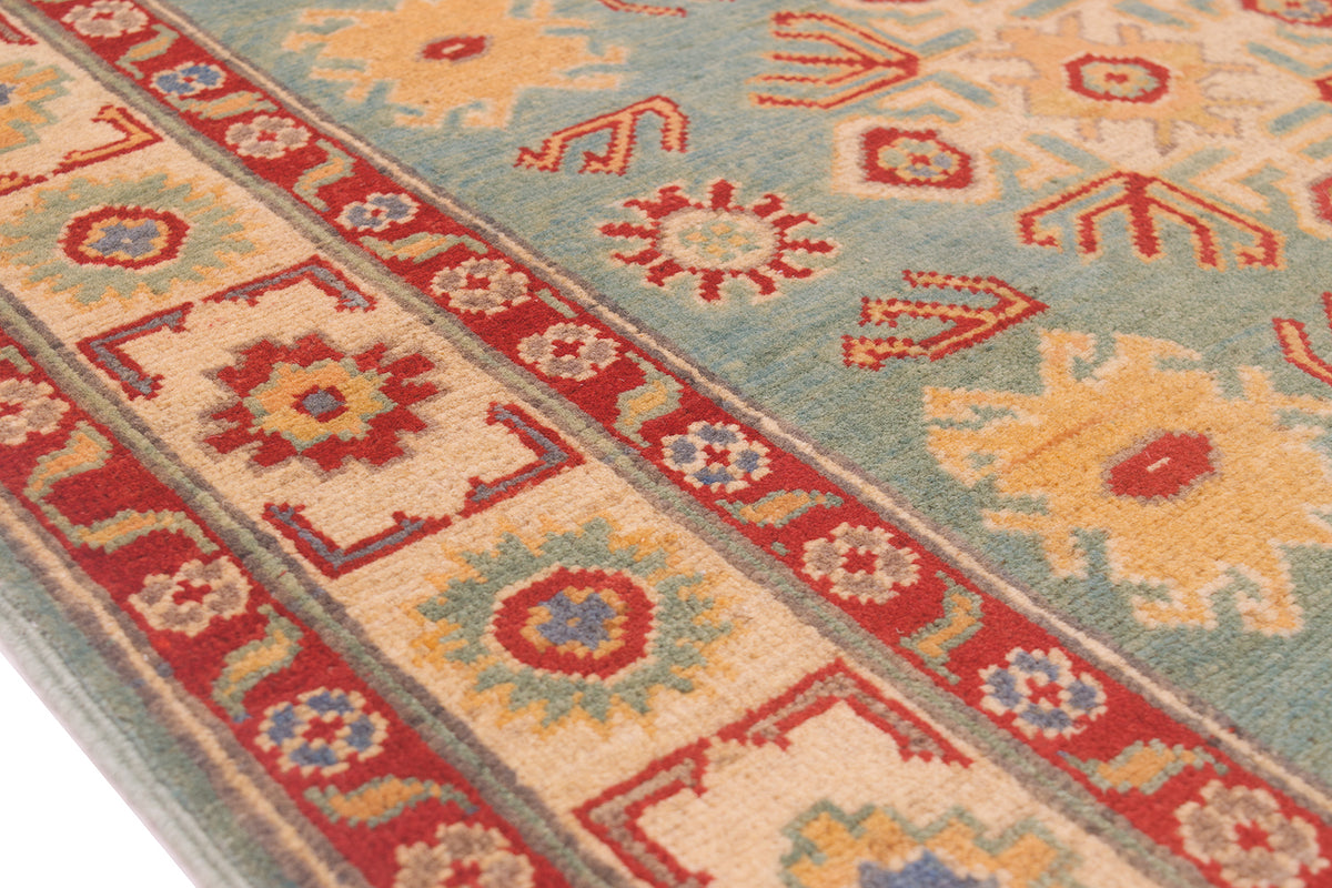 A close-up of a patterned Afghan Kazak wool rug with a light sea-green field, red borders, and cream floral motifs.