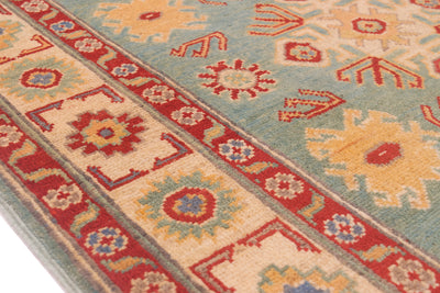 A close-up of a patterned Afghan Kazak wool rug with a light sea-green field, red borders, and cream floral motifs.