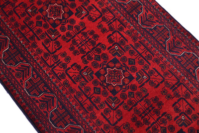 A close-up of a red patterned rug with dark navy geometric and floral motifs, shown diagonally against a white background.