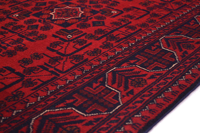 A close-up of a red and black patterned runner rug with geometric and floral motifs, showing the detailed woven texture and border design.