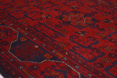 A close-up of a traditional afghan runner rug with a deep red field, dark navy blue borders, and small orange and beige floral accents.