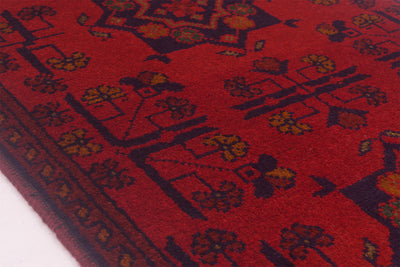 A close-up of a red patterned afghan rug with dark navy and mustard yellow geometric and floral motifs.