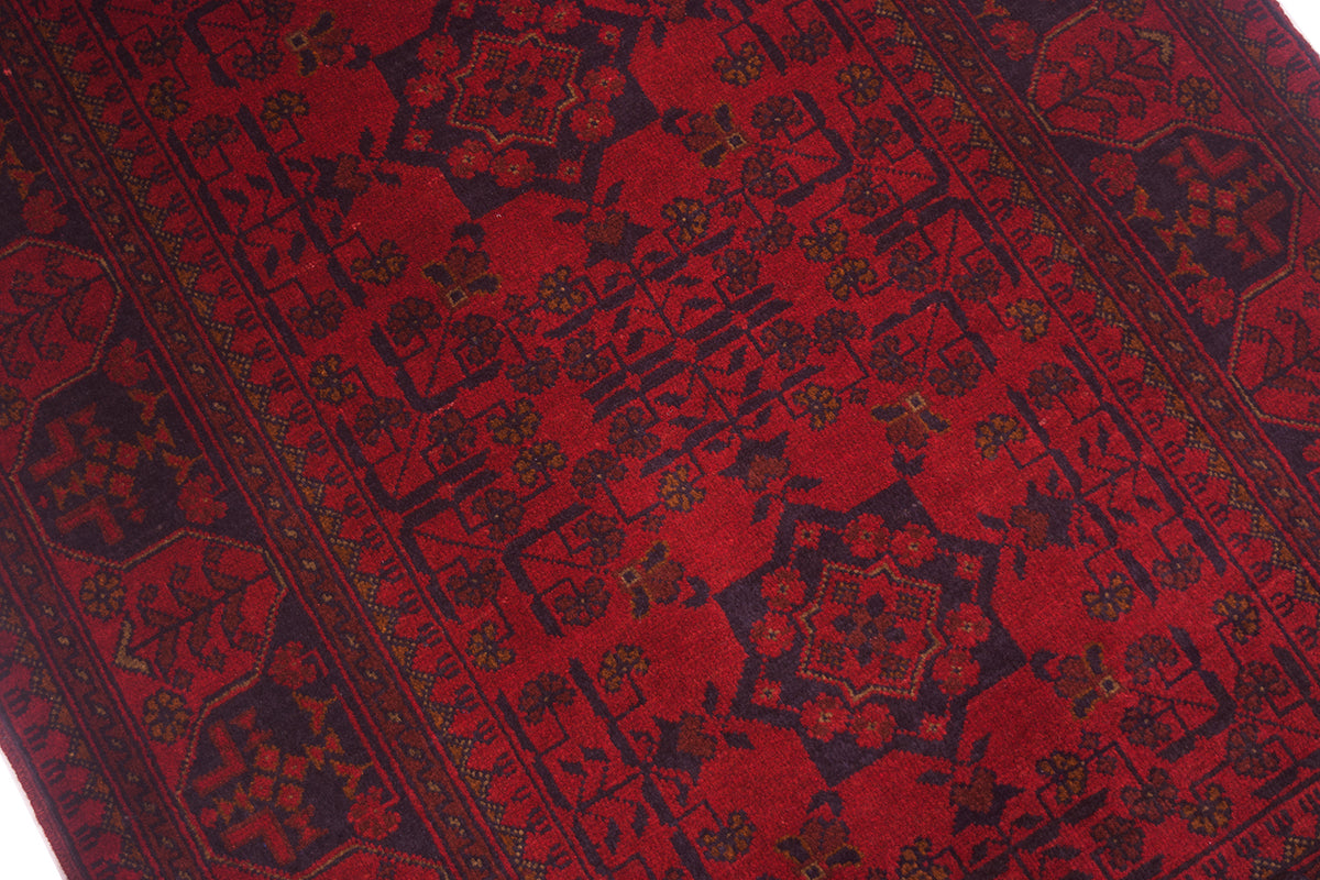 A close-up of a traditional afghan patterned rug with a deep red field, dark navy borders, and small floral accents.