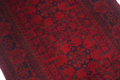 A close-up of a traditional afghan patterned rug with a deep red field, dark navy borders, and small floral accents.