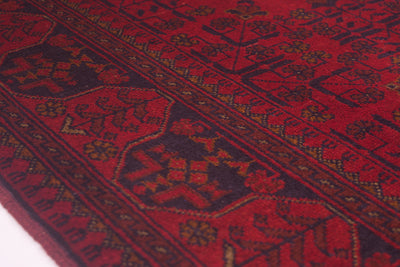 A close-up of a red afghan patterned rug with dark brown and black geometric motifs and borders.
