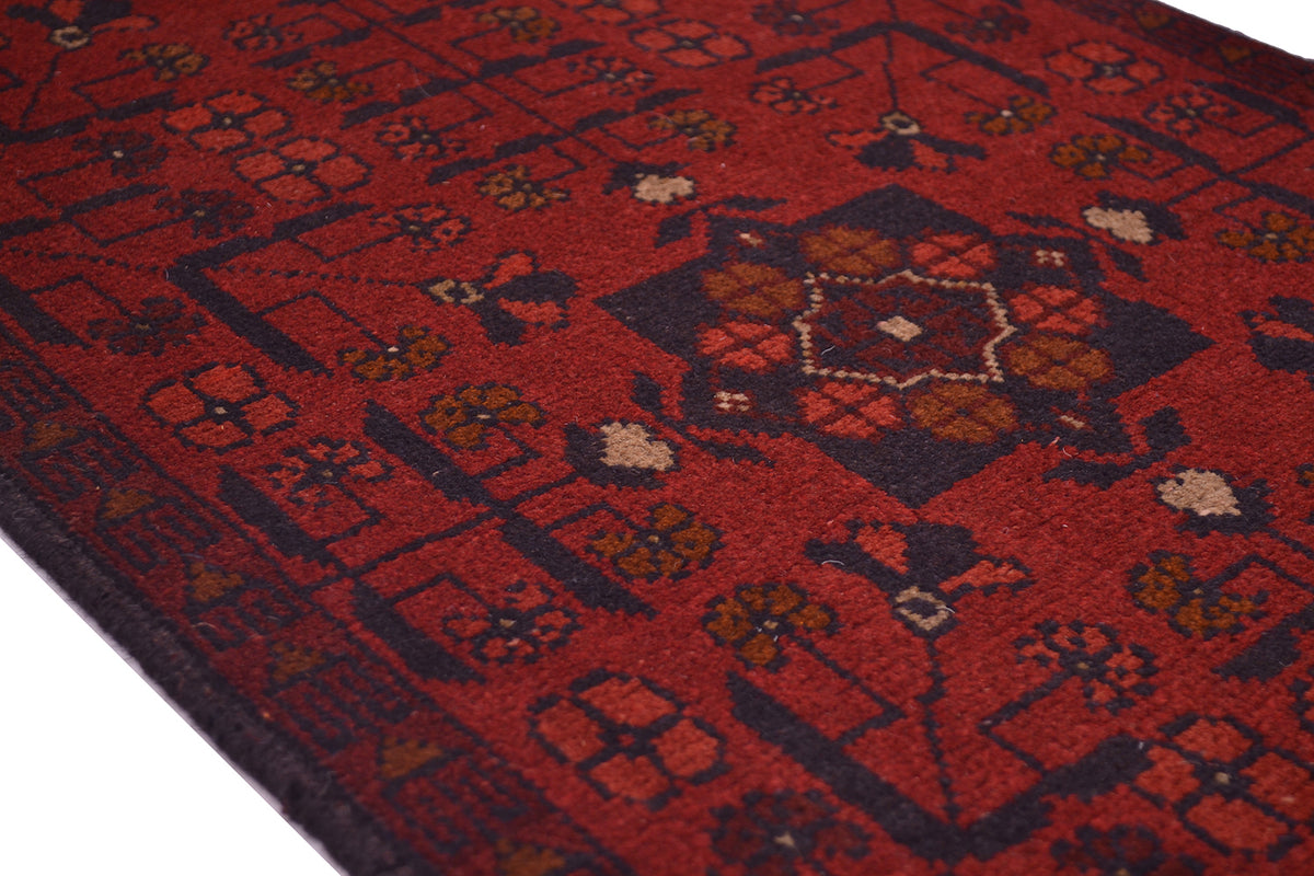 A close-up of a patterned afghan area rug runner with a deep red field, dark navy geometric borders, and central medallions in brown, beige, and muted orange.
