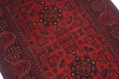 A close-up of a traditional Afghan  patterned rug with a deep red field, dark  borders, and intricate geometric and floral motifs in black, brown, and beige.