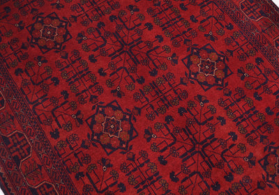 A close-up of a red handmade rug with dark navy blue geometric and floral motifs, bordered on the left side.