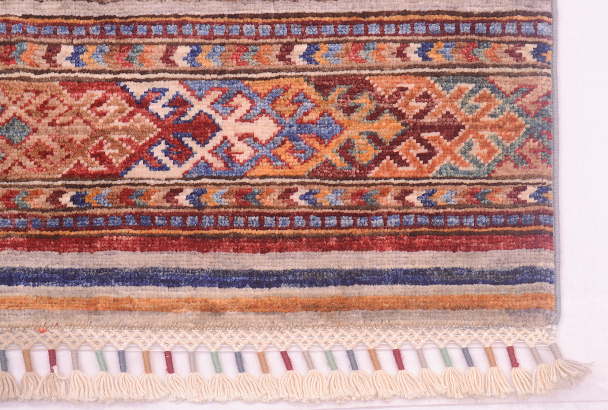 A close-up of a patterned Khorjin Afghan runner rug with geometric bands in red, blue, orange, beige, and brown, finished with cream fringe along the bottom edge.