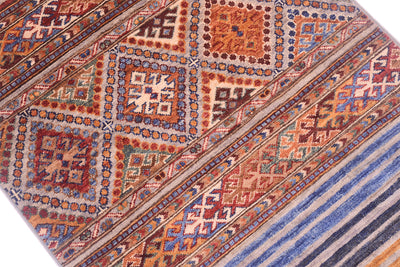 A close-up of a patterned Khurjeen design runner with geometric tribal designs in rust red, blue, beige, and brown tones.