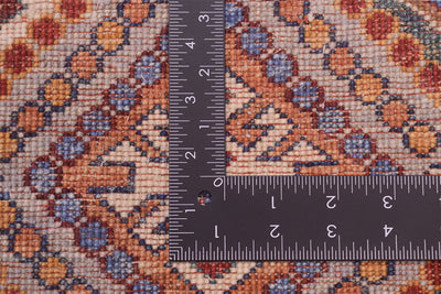 A close-up of the hand-knotted back of an Afghan Khorjin patterned runner with a dark metal ruler placed at the corner to show the scale of its knot density. The fabric features a detailed geometric and floral design in rust orange, blue, beige, and brown.