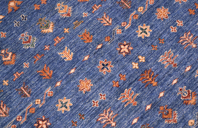 A close-up of a blue patterned Afghan Khorjin carpet with repeating floral and geometric motifs in rust orange, beige, and small green accents.