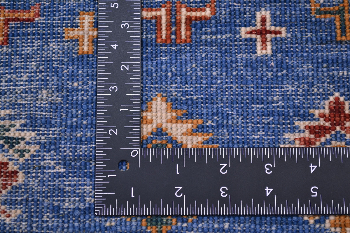Close-up of the hand-knotte weave of a blue Afghan Khorjin carpet with geometric motifs in orange, cream, and red, shown with a black L shaped ruler to indicate scale of the knot density.
