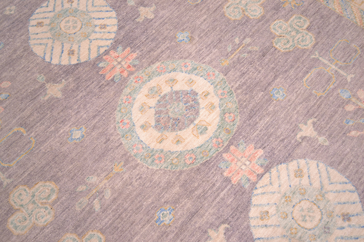 Close up detail of made field of Khotan design carpets with main field of soft dove grey with three moon gul medallions in cream, green, blue and coral pinks.  Numerous semi geometric motifs spaciously placed in field. 
