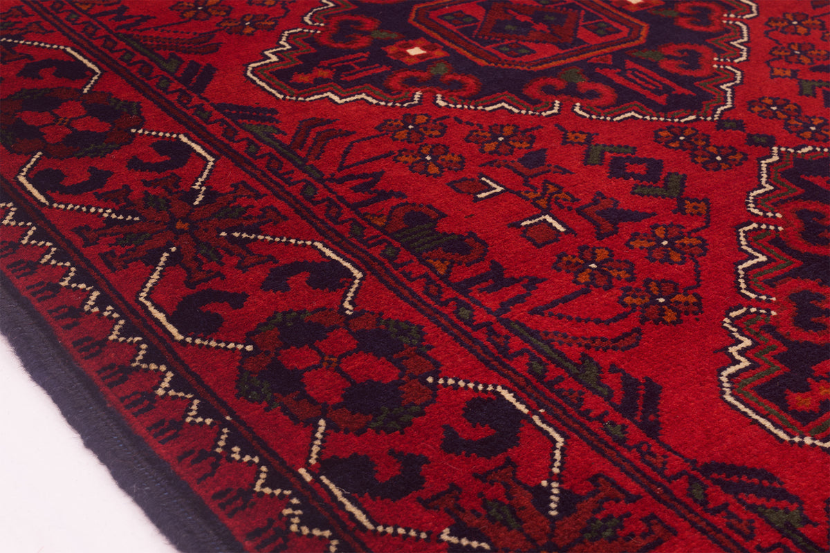 A close-up of a traditional afghan patterned runner with a deep red field, dark navy borders, and cream and olive accents, shown on a white surface.