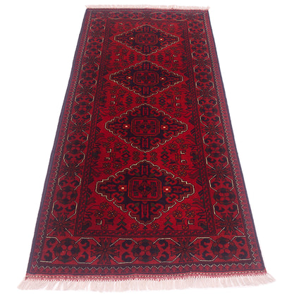 A traditional afghan runner rug with a deep red field, dark navy blue geometric medallions, and cream-colored fringe on the ends.