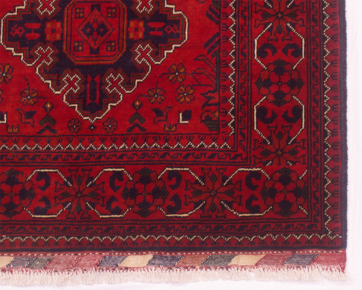 A close-up of a red runner rug corner showing a central medallion, decorative borders, and a fringed edge on a white background.