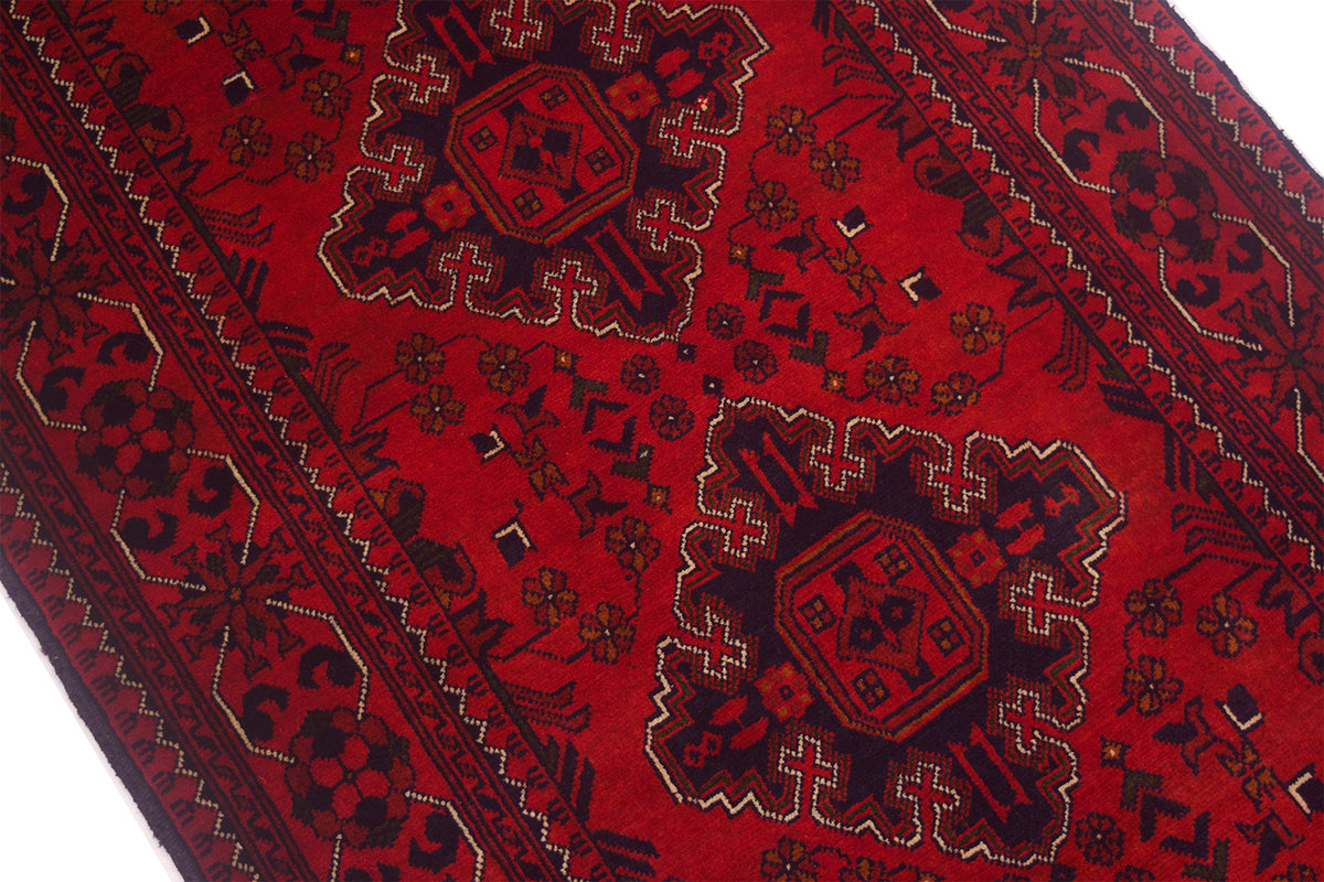 A close-up of a red afghan runner rug with dark navy and beige geometric medallions and floral motifs.