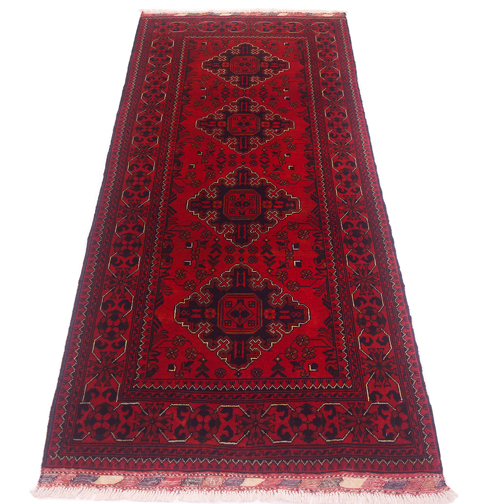 A traditional afghan runner rug with a deep red field, featuring four central medallions in black, surrounded by ornate borders in black and finished with white fringe on the ends.