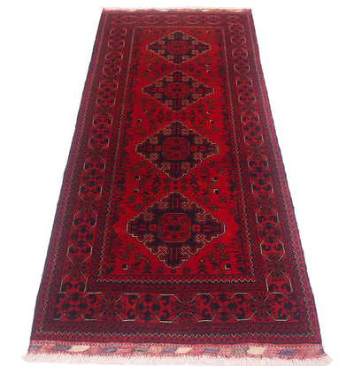 A traditional afghan runner rug with a deep red field, featuring four central medallions in black, surrounded by ornate borders in black and finished with white fringe on the ends.