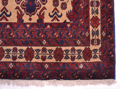 A close-up of a traditional runner rug corner showing a beige field with red and navy floral motifs and a red border with cream fringe.