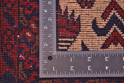 Close-up of back of a patterned afghan runner rug with a metal ruler placed along the edge to show scale, featuring a red, navy, and beige woven design.