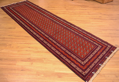 A long runner rug with a traditional geometric pattern in red, navy, and beige, laid out diagonally on a light wood floor.