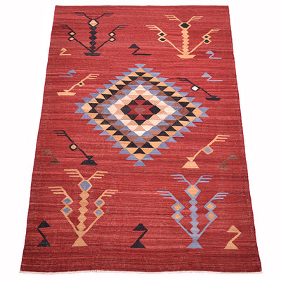 A rectangular handwoven red Labijar Kilim rug with a Southwestern geometric pattern, featuring a large central diamond and stylised tree motifs in beige, blue, black, and red.