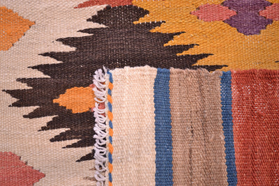 Close-up of the back of a handwoven Labijar Kilim runner with a geometric pattern in beige, black, orange, purple, blue, and red, showing a fringed edge.