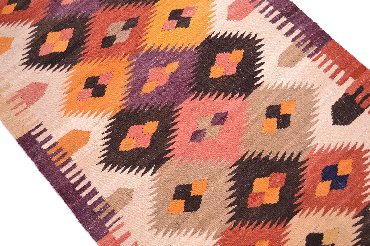 A close-up of a handwoven Labijar Kilim runner with a geometric Southwestern-style pattern in orange, pink, purple, brown, and beige on a white background.