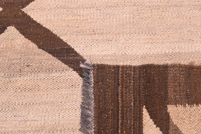 Close-up of a tribal style handwoven Afghan Kilim showing a geometric pattern in dark brown and beige with a fringe edge.