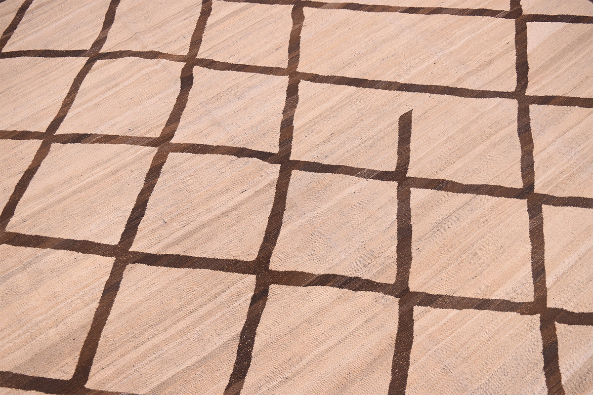 A close-up of a Tribal style handwoven Afghan Kilim with a light beige base and a dark brown grid pattern.