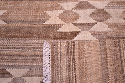 Close-up of the weave of a handwoven Afghan Kilim rug with a geometric pattern in shades of brown, beige, and cream, featuring a white fringed edge.