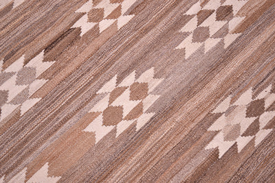 A close-up of a handwoven natural Labijar Kilim rug with a geometric diamond pattern in shades of brown, beige, and cream, showing the detailed texture of the weave.