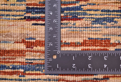 Close-up of the hand-knotted back of an Afghan Gabbeh rug with horizontal stripes in beige, blue, rust orange, and brown, shown with a black metal ruler to show scale of the knotting.