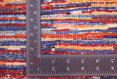 Close-up of the hand-knotted back of a modern Stripy Gabbeh rug with red, blue, orange, and cream bands, shown with a dark metal L-shaped ruler to show scale of the knot density.