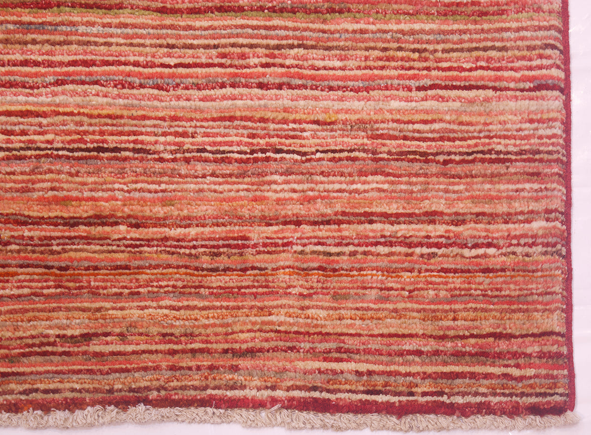 A close-up of a handwoven Gabbeh rug with horizontal textured stripes in shades of rust red, terracotta, orange, and beige.