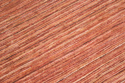 A close-up texture shot of a handwoven Afghan Gabbeh carpet featuring stripes in warm rust red, terracotta, and brown tones.