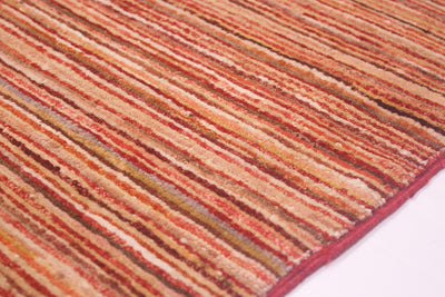 A close-up of a textured Afghan stripy Gabbeh rug featuring a striped pattern in warm tones of rust red, orange, beige, and brown, with a solid red selvedge edge visible on the bottom right.