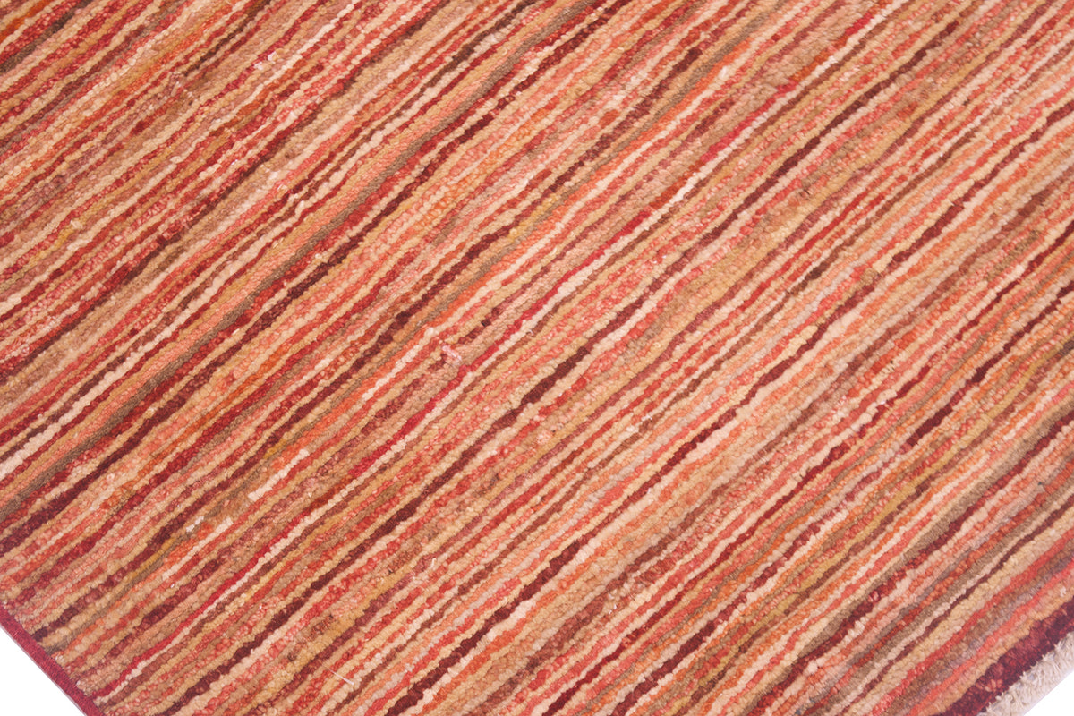 A close-up of a Gabbeh rug featuring narrow stripes in warm rust red, terracotta, orange, and brown tones.