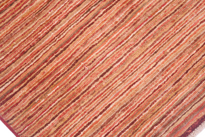 A close-up of a Gabbeh rug featuring narrow stripes in warm rust red, terracotta, orange, and brown tones.
