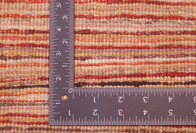 Close-up of the hand-knotted weave of a striped Afghan Gabbeh carpet in warm earthy tones, shown with a dark metal L-shaped ruler to indicate scale of the knotting.