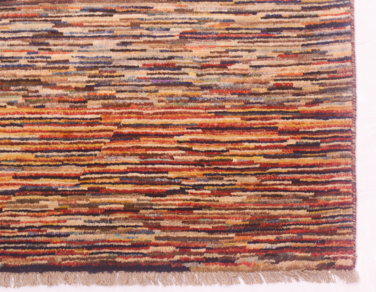 A close-up of a 3x2m handmade modern Afghan Gabbeh carpet showing its detailed woven pattern with horizontal stripes in rust orange, beige, brown, and dark navy, finished with a fringed edge.