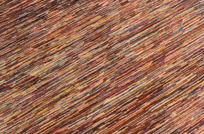 A close-up of Handmade modern Afghan Gabbeh carpet featuring diagonal stripes in a multicolour pattern of rust red, brown, beige, and muted blue.