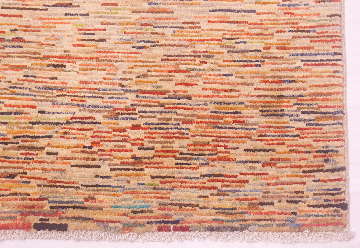 A close-up of a handmade Afghan Gabbeh carpet with horizontal multicolour stripes in orange, red, blue, and brown on a cream base, finished with a fringed edge.