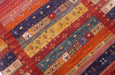 A close-up of a colourful geometric patterned Afghan Loribaft rug with diagonal stripes in red, orange, mustard yellow, teal blue, and navy, featuring intricate tribal-style motifs.