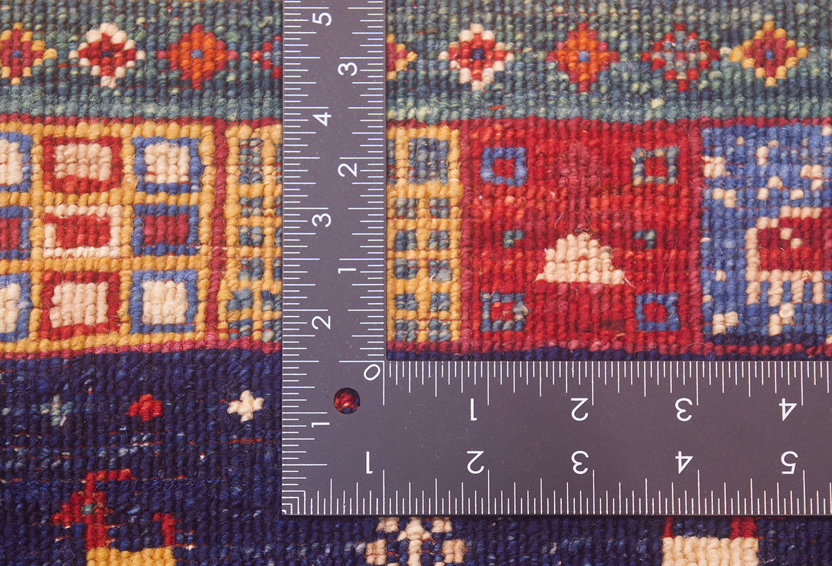 A close-up of a hand-knotted back of a Afghan colourful Loribaft rug with a dark metal ruler placed vertically and horizontally to show the scale of the fineness of the knotting.